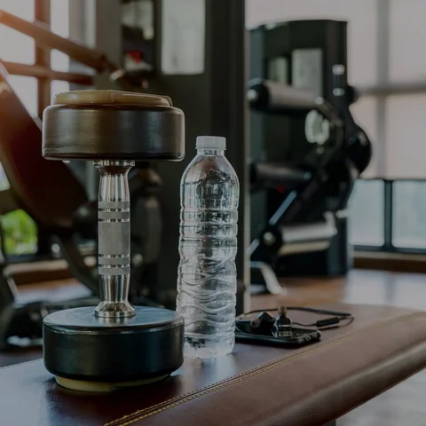 Fotografía pesa y botella de agua sobre una banca de ejercicio dentro de un gimnasio